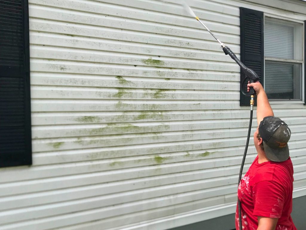 Worker pressure washing the exterior siding of a residential home